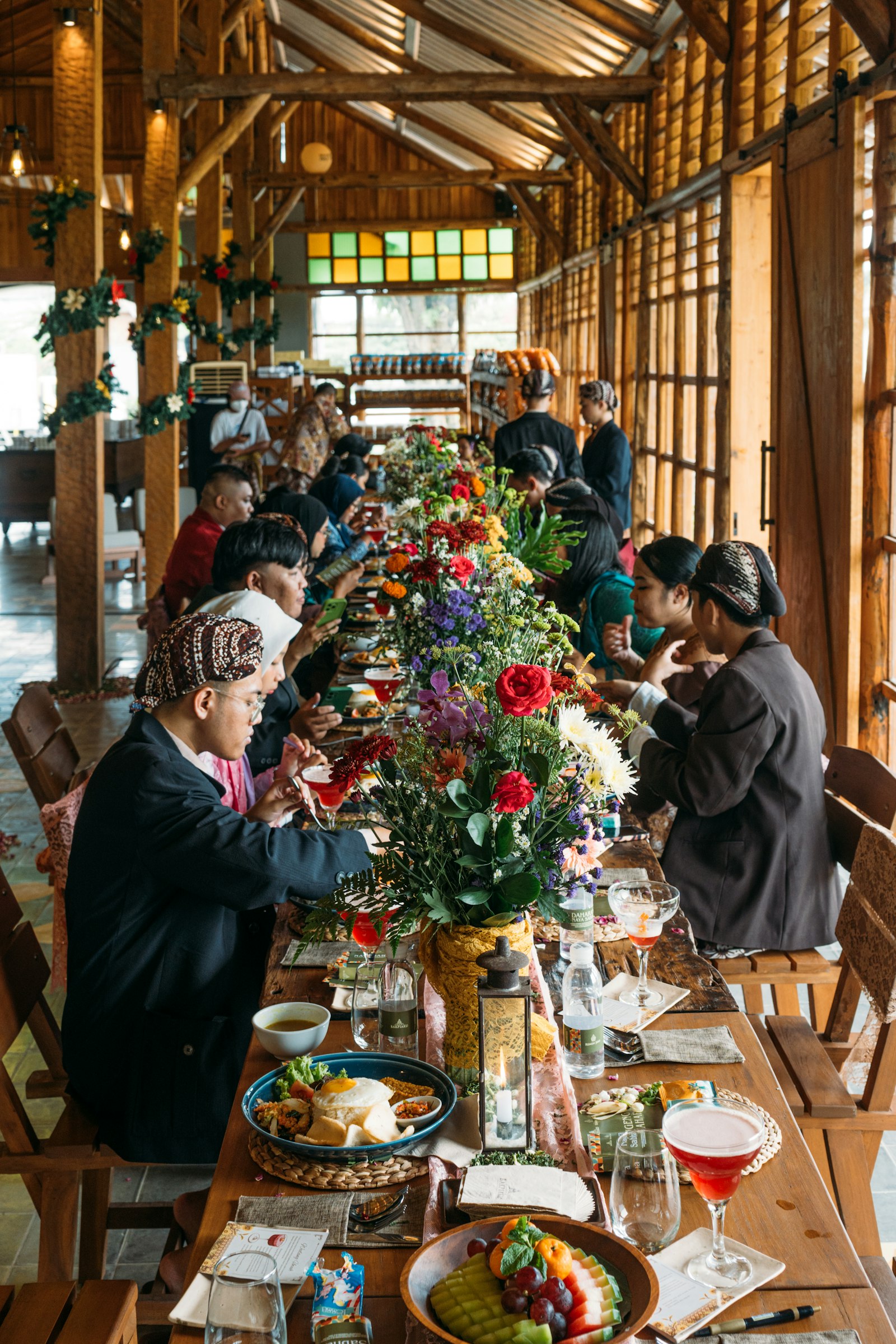 Mesa larguísima decorada con flores, llena de comensales